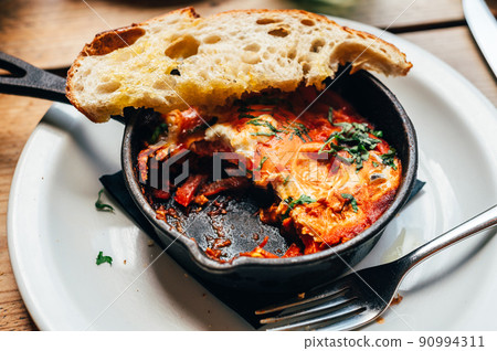 Shakshuka in iron pan served with bread 90994311
