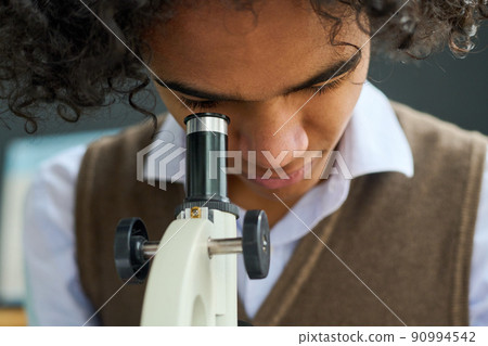 Close-up of teenage guy studying chemical or biological substance in microscope Close-up of teenage guy studying chemical or biological substance in microscope 90994542