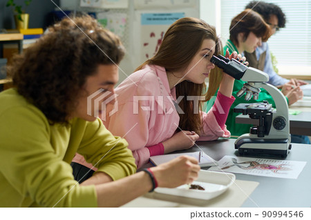 Teenage girl in casualwear studying dissected part of frog in microscope Teenage girl in casualwear studying dissected part of frog in microscope 90994546