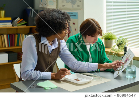 African American student pointing at paper with sketch of frog held by girl 90994547