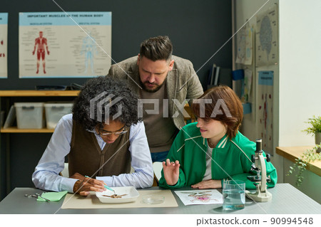 Mature male teacher of anatomy bending over two students during frog dissection Mature male teacher of anatomy bending over two students during frog dissection 90994548
