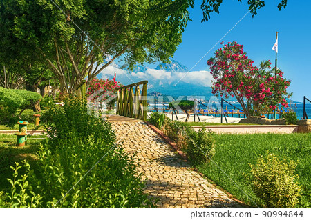 View of the path and the bridge in a green garden with green trees along the embankment in Kemer, Turkey. 90994844