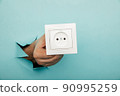Male hand holds socket in torn hole of blue background 90995259