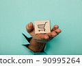 Hand with a delivery box through a blue paper hole 90995264