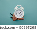 Hand holds alarm clock through a blue paper hole. Time management and deadline concept 90995268