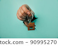 Man's hand with house key through a hole in blue background. House sale and rent concept 90995270