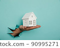Man's hand with house through a hole in blue paper. House sale and rent concept 90995271