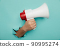 Man's hand arm hold megaphone isolated through torn blue background 90995274