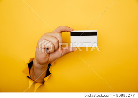 Male hand is holding credit bank card in torn hole of yellow background. Online shopping, purchasing products concept. 90995277