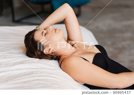 an attractive brunette woman in a black bodysuit by the bed in the bedroom. an attractive brunette woman in a black bodysuit by the bed in the bedroom. 90995437