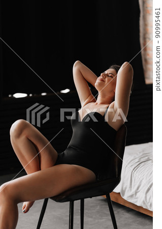 an attractive woman in a black bodysuit on a chair in the bedroom.  90995461