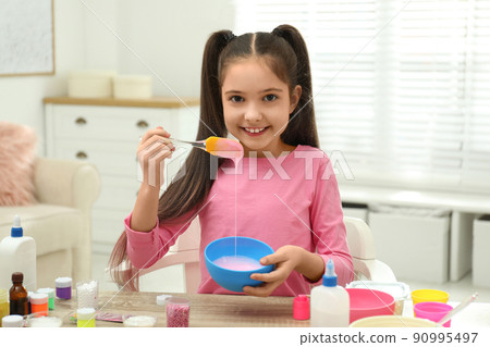 Cute little girl mixing ingredients with silicone spatula at table. DIY slime toy Cute little girl mixing ingredients with silicone spatula at table. DIY slime toy 90995497