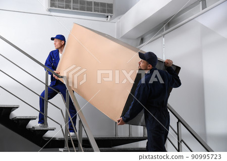 Professional workers carrying refrigerator on stairs indoors Professional workers carrying refrigerator on stairs indoors 90995723