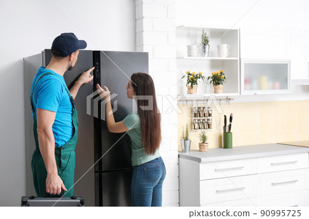 Male technician talking with client near refrigerator in kitchen Male technician talking with client near refrigerator in kitchen 90995725