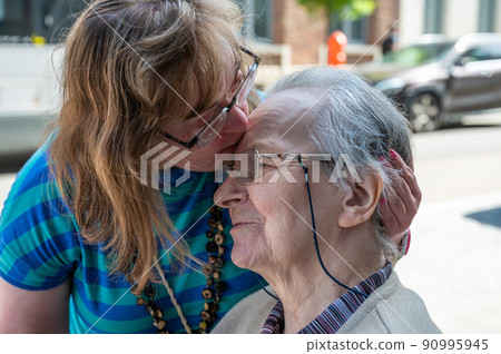 Cheerful moment between an 83 year old senior woman kissing her 39 year old daughter with the Down Syndrome Cheerful moment between an 83 year old senior woman kissing her 39 year old daughter with the Down Syndrome 90995945