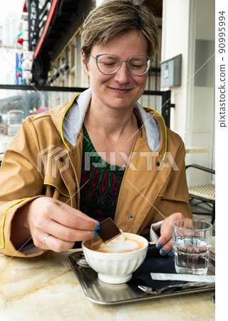 Portrait of a 35 year old white woman sitting on a terrace, drinking coffee with chocolates 90995994