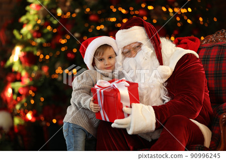 Santa Claus and little boy with gift near Christmas tree indoors 90996245