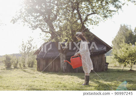 Young female gardener watering the plants in the garden in summer. Young woman with a watering can 90997245