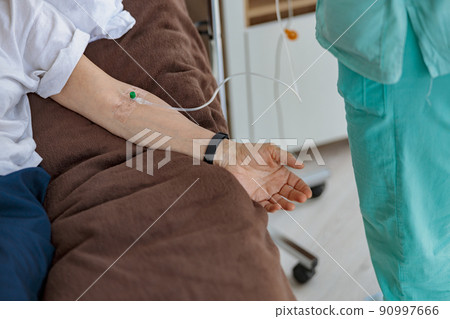Nurse putting a drip in the arm of her patient in modern medical clinic Nurse putting a drip in the arm of her patient in modern medical clinic 90997666