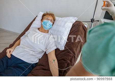 Nurse putting a drip in the arm of her patient in mask during covid-19 epidemic 90997668