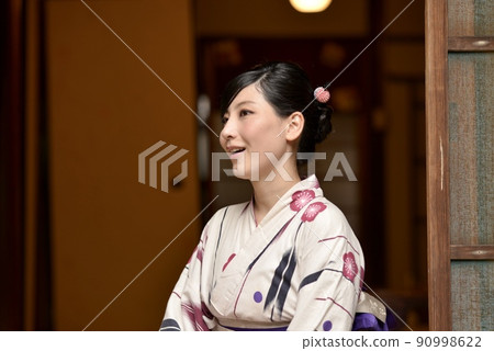 一位穿著浴衣的年輕女子坐在町屋的門廊上微笑著 一位穿著浴衣的年輕女子坐在町屋的門廊上微笑著 90998622