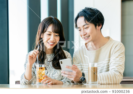 一對年輕夫婦在咖啡館看智能手機 一對年輕夫婦在咖啡館看智能手機 91000236