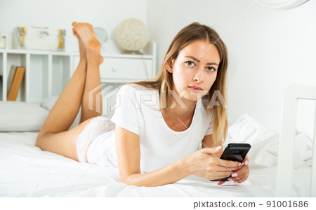 Girl texting on phone in bed 91001686