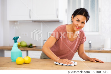 Smiling woman cleaning table with rag at home 91001819
