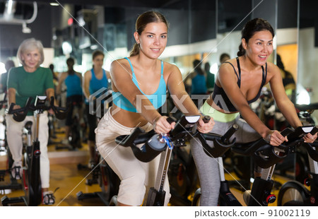 Women training on stationary bikes at gym 91002119