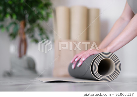 Close-up of a woman's hands rolling up an exercise mat. Yoga studio. Concept of a healthy lifestyle. Close-up of a woman's hands rolling up an exercise mat. Yoga studio. Concept of a healthy lifestyle. 91003137