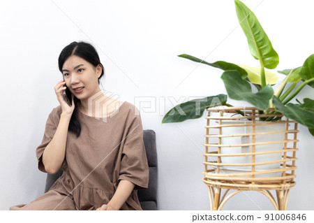 Young Asian woman happily using her mobile phone to chat or talking with her friends, Entertaining or relaxing using mobile phone technology, Stay at home for long weekend, Happy lifestyle. 91006846