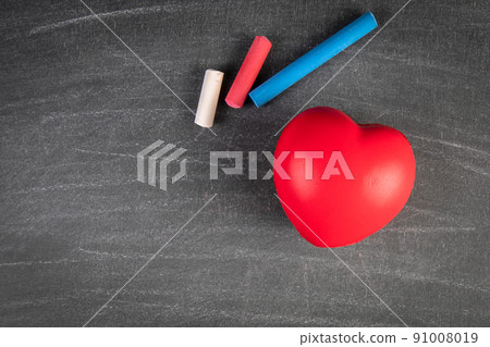 Red rubber heart and chalk pieces on a blackboard. Copy Space 91008019