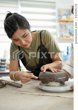 A beautiful Asian woman making moulding clay plate, making a ceramic plate 91009135