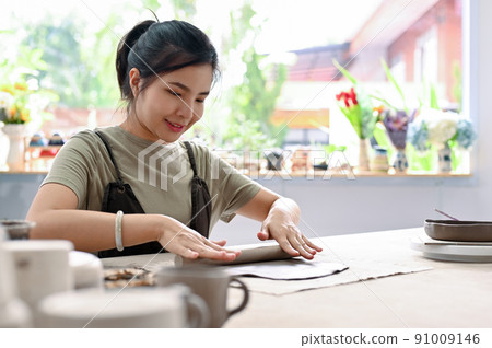Asian woman relaxes rolling clay on worktable in the handcraft workshop. Moulding pottery. Asian woman relaxes rolling clay on worktable in the handcraft workshop. Moulding pottery. 91009146