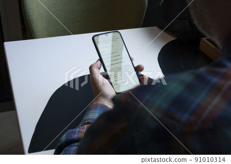 a man holding a smartphone in his hand is looking at the photographer from behind his shoulder from behind a man holding a smartphone in his hand is looking at the photographer from behind his shoulder from behind 91010314