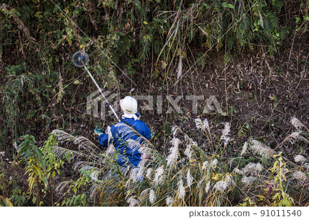 A planter who cuts thickly overgrown weeds with an electric mower 91011540