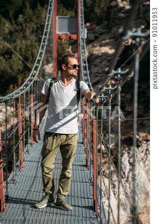 Portrait of middle-aged hiker passing by the hanging bridge and looking away. Travel concept Portrait of middle-aged hiker passing by the hanging bridge and looking away. Travel concept 91011953