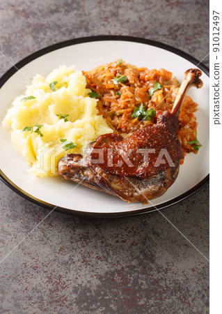 Baked duck leg serving with mashed potatoes and stewed cabbage close-up in a plate. Vertical 91012497