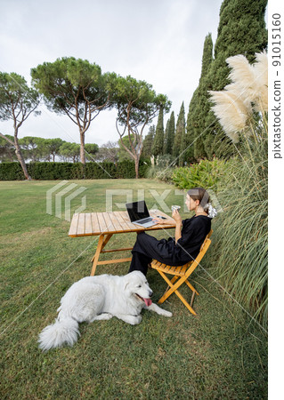 Girl caress dog and use laptop at table on lawn Girl caress dog and use laptop at table on lawn 91015160