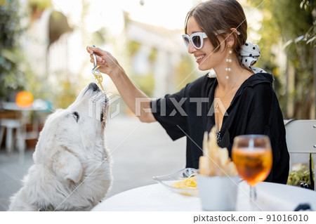 Woman eating pasta with her cute white dog at the restaurant Woman eating pasta with her cute white dog at the restaurant 91016010