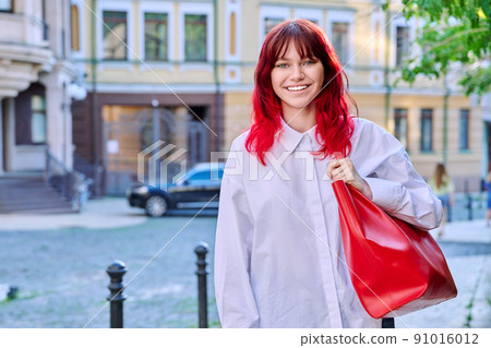 Teenage fashionable smiling female with red dyed hair looking at camera Teenage fashionable smiling female with red dyed hair looking at camera 91016012
