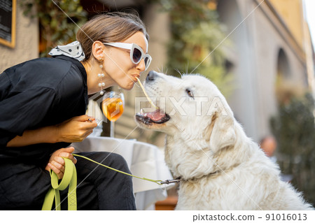 Woman eating pasta with her cute white dog at the restaurant Woman eating pasta with her cute white dog at the restaurant 91016013