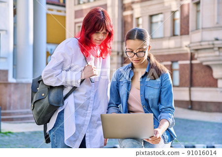 Two teenage female students using outdoor laptop, city street background Two teenage female students using outdoor laptop, city street background 91016014