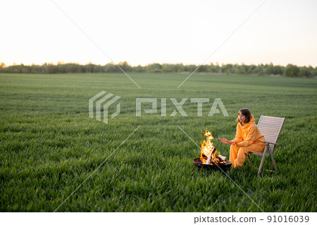 Woman sitting by the fireplace on green field on sunset 91016039