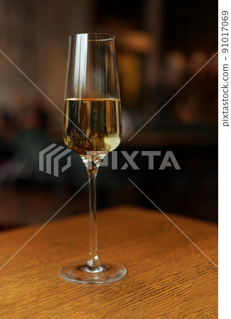 Glass of champagne standing on wooden table in soft focus on naturally blurred dark background. White wine with bubbles. Celebration, happy holidays concept 91017069