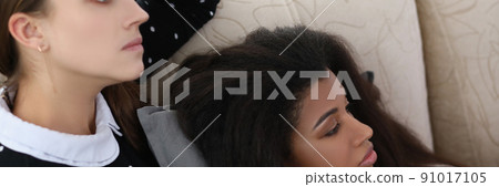 Brunette woman and her latino american friend watch television at home on couch 91017105