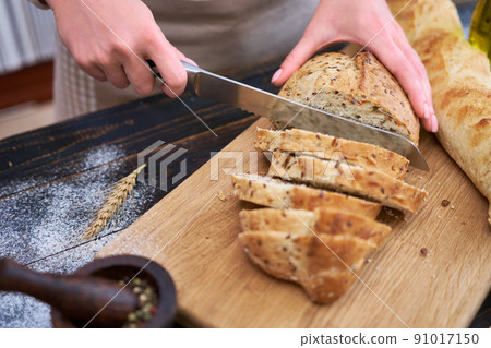 Woman cutting freshly baked bread at wooden kitchen table 91017150
