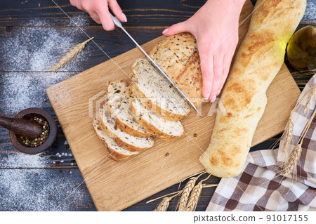 Woman cutting freshly baked bread at wooden kitchen table Woman cutting freshly baked bread at wooden kitchen table 91017155
