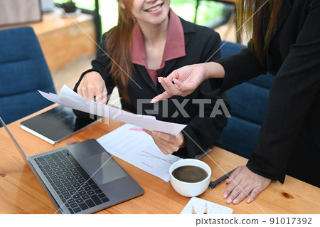 Cropped view of two business women discussing over marketing data report financial results at office desk Cropped view of two business women discussing over marketing data report financial results at office desk 91017392