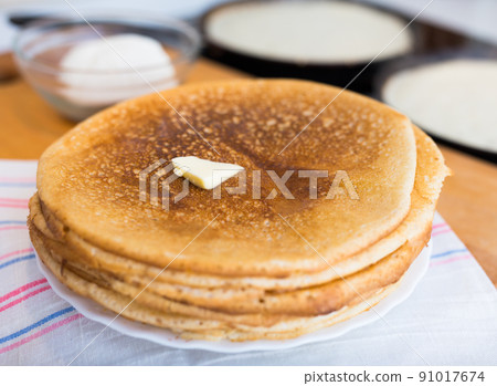 hot golden pancakes made from grain flour in kitchen while cooking on pans and on plate 91017674